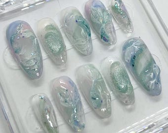 May include: A set of ten false nails with a white and light blue design. The nails are arranged in a clear plastic case.