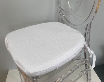 Puede incluir: Cojín de silla blanco con una superficie de tela texturizada. El cojín se coloca en una silla de plástico transparente con un respaldo decorativo.
