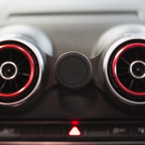 Puede incluir: Primer plano del salpicadero de un coche con dos salidas de aire con ribete rojo y un soporte de teléfono negro en el centro.