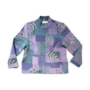 May include: A long-sleeved jacket with a patchwork design in shades of purple, green, and gray. The jacket features floral and leaf patterns, a mandarin collar, and a zipper closure. The fabric has a textured appearance.