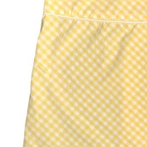 May include: Close-up of a yellow and white gingham fabric. The fabric is a classic checkered pattern, with a small white border at the top. The fabric is likely cotton or a similar material, and is suitable for clothing or home decor.