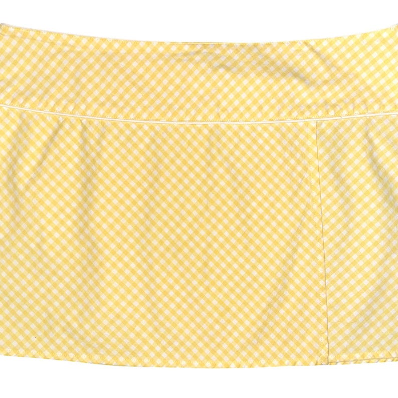 May include: A yellow and white gingham skirt. The skirt has a straight cut and a white trim along the waistband. The fabric is a classic checkered pattern, with a light yellow and white color scheme.