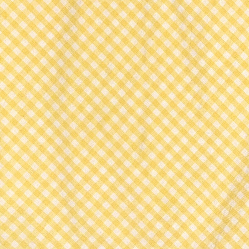 May include: A close-up of a yellow and white gingham pattern. The fabric has a repeating square design in a diagonal orientation. The yellow squares are a soft, muted tone, and the white squares are a bright, clean white.