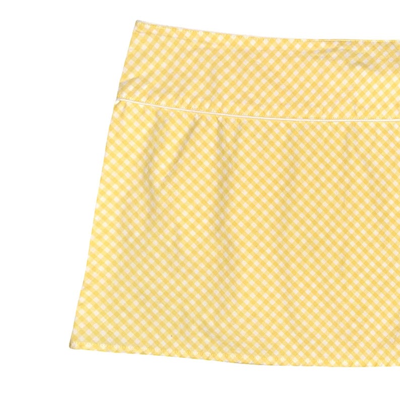 May include: A yellow and white gingham pattern skirt. The skirt has a classic checkered design, with a white trim along the top edge. The fabric is a light, summery material.