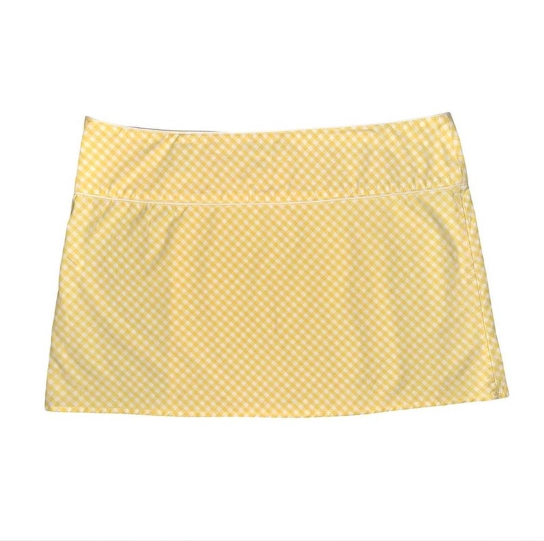 May include: A yellow and white gingham pattern skirt. The skirt has a straight cut and a white trim along the top edge. The fabric is a light, summery material.