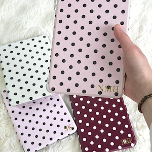 May include: Three rectangular tablet cases featuring polka dot patterns in light pink, white, and dark maroon. Each case displays gold-colored monogrammed initials at the bottom right corner, specifically reading NMH, SK, and BSF respectively.