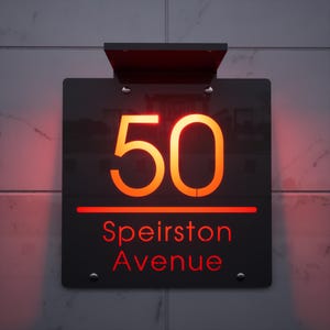 May include: A black address sign with the number "50" in orange illuminated letters. Below the number is a red line, and the words "Speirston Avenue" are written in red. The sign is mounted on a wall.