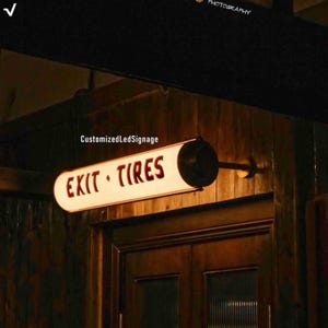 Könnte beinhalten: Ein beleuchtetes Schild im Vintage-Stil mit den roten Worten "EXIT TIRES". Das Schild hat eine ovale Form mit cremefarbenem Hintergrund und schwarzen Enden. Es ist über einer Holztür montiert.