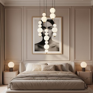 May include: A bedroom scene featuring a bed with neutral-toned bedding, flanked by bedside tables with spherical lamps. Above the bed hangs a framed black and white portrait, and a cluster of pendant lights with spherical, glowing bulbs.