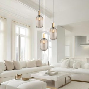 Peut inclure: Trois lampes suspendues dorées avec des abat-jours en verre côtelé transparent pendent du plafond dans un salon moderne aux murs blancs et un canapé blanc.