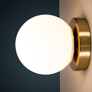 May include: A gold wall sconce with a white frosted glass globe. The sconce has a brushed metal finish.