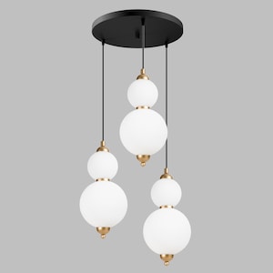 May include: A modern pendant light fixture with three white globe shades suspended from a black circular canopy. The shades are accented with gold-colored hardware. The light fixture is designed for indoor use and adds a touch of elegance to any room.