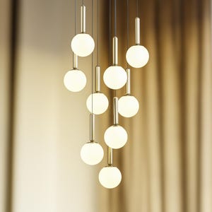 Könnte beinhalten: Eine moderne goldene Pendelleuchte mit neun weißen, kugelförmigen Schirmen, die in unterschiedlichen Längen hängen.