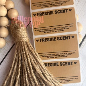 May include: A stack of brown rectangular labels with the text "FRESHIE SCENT" and safety instructions. A jute tassel and wooden bead garland are in the image.