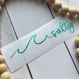 May include: A teal green glitter wave design with the text "Salty" in cursive script on a white background.