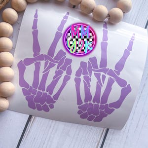 May include: A light purple vinyl decal featuring two skeleton hands making peace signs. A circular logo is positioned between the hands, displaying a black and white checkered pattern with the text MM Y2K in bright pink, blue, and yellow letters.