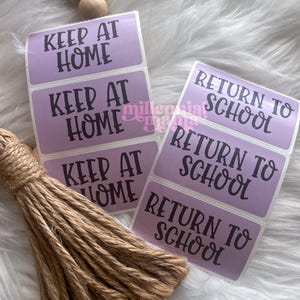 May include: A collection of lavender rectangular labels with black text. The labels read "KEEP AT HOME" and "RETURN TO SCHOOL". A bundle of brown twine and wooden beads are also in the image.