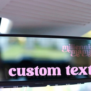 May include: Pink car mirror with a pink and white sticker that says "millennial mama" and a pink sticker that says "custom text".