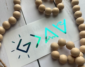 May include: A teal holographic vinyl decal featuring the text G > ^ v, with the G stylized as a sun, the > as a greater than sign, the ^ as a mountain peak, and the v as a wave. The decal is surrounded by a long strand of natural wooden beads.