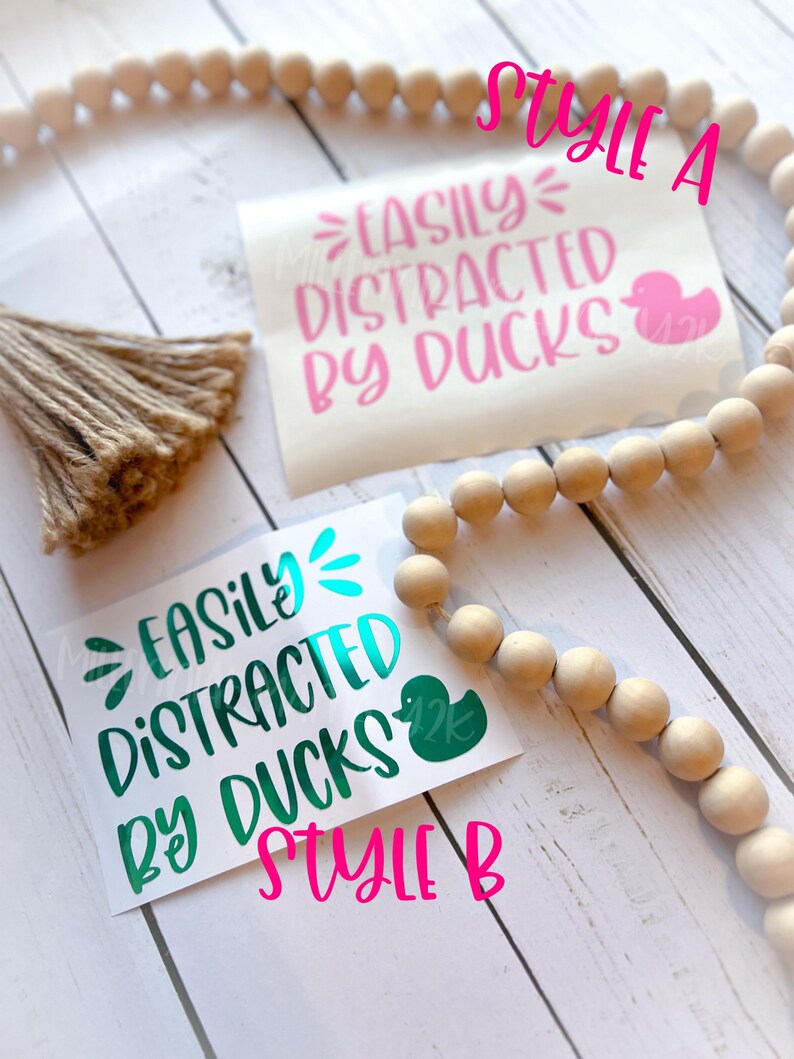 May include: Two versions of a vinyl sticker with the text "Easily Distracted by Ducks" and a rubber duck graphic. The top sticker is pink and the bottom sticker is teal.