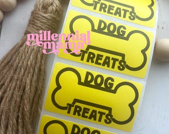 May include: A sheet of yellow dog treat labels with a bone shape. Each label has the words "DOG TREATS" in black. The labels are on a white background with wooden beads and a tassel.