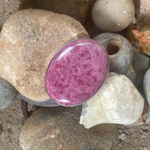 May include: A pink and white oval-shaped stone set in a silver ring. The stone has a marbled pattern and is surrounded by a smooth silver band.