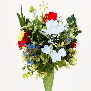 May include: A floral arrangement featuring red roses, white blossoms, and small blue flowers mixed with green foliage. The bouquet is contained within a textured, cone-shaped green base, creating a vibrant display of assorted artificial plant life.