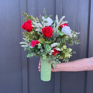 May include: A green vase filled with a bouquet of red and white roses and greenery.