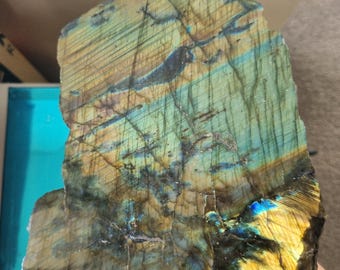 May include: A large, rough-hewn piece of labradorite with iridescent blue, green, and gold colors. The stone has a natural, unpolished finish.