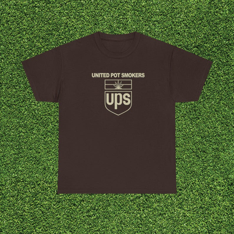May include: A brown t-shirt with the text "UNITED POT SMOKERS" above a logo that resembles the UPS logo, but with a cannabis leaf and the letters "ups". The shirt is displayed on a green surface.