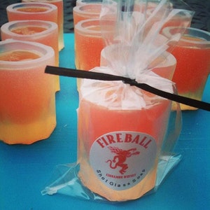 May include: Orange-colored shot glass soaps, some in a clear plastic bag, with a "Fireball Cinnamon Whisky Shot Glass Soap" label. The soaps are arranged on a blue surface.