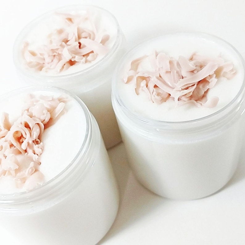 May include: Three white jars with clear lids filled with a white cream and topped with pink, shredded coconut flakes.