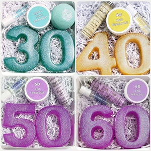 May include: Four gift boxes with different colored numbers, each box contains bath products and a small jar with a message. The boxes are decorated with white shredded paper. The numbers are 30, 40, 50, and 60. The jars say "Happy 30th Birthday!" "40 and Fabulous!" "50 and Fabulous!" and "60 and Fabulous!"