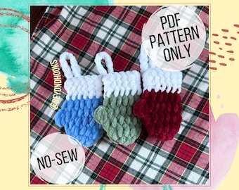 May include: Three crocheted mitten ornaments in blue, green, and red with white tops. The ornaments are on a red and white plaid fabric. The text "PDF PATTERN ONLY" and "NO-SEW" are on the image.