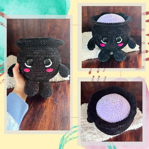 May include: A black crocheted cauldron plush toy with a purple lining and googly eyes. The cauldron has a cute, cartoon-like face with pink cheeks.