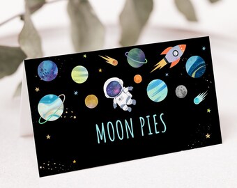 May include: A black card with a space theme featuring planets, stars, a rocket, and an astronaut. The text "MOON PIES" is printed in white on the card.