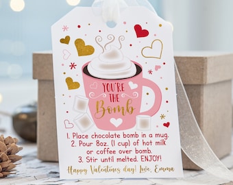 May include: A Valentine's Day gift tag with a pink mug design that says "You're the Bomb." The tag includes instructions for making a hot chocolate bomb, with hearts and gold accents. A white ribbon is attached.