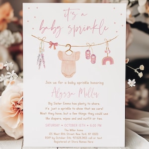 以下が含まれることがあります： 水彩イラストのベビーシャワー招待状。「it's a baby sprinkle」というテキストがピンク色の筆記体で書かれ、ベビーをテーマにした装飾が施された物干しロープが描かれています。招待状には、Alyssa Millerの名前とイベントの詳細が含まれています。