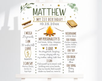 May include: A white printable sign with a campfire theme for a first birthday. The sign has a gold background with the name "MATTHEW" and the text "MY 1ST BIRTHDAY 10.25.20XX". The sign lists details about the child, including their weight, height, favorite foods, toys, and songs.