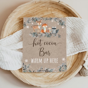 K&ouml;nnte beinhalten: Ein braunes Schild mit wei&szlig;em Hintergrund und einem winterlichen Waldmotiv. Es steht "hot cocoa bar" und "warm up here" mit einer Illustration von einem Reh, Fuchs, Eule und Waschb&auml;r.