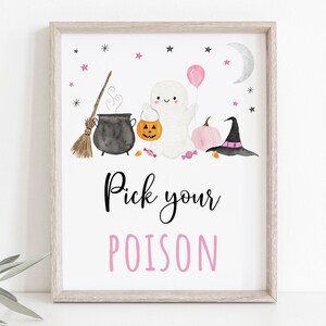 May include: A white framed printable sign with a pink and black Halloween theme. The sign features a ghost, a cauldron, a broom, a pumpkin, a witch's hat, and candy. The text on the sign reads "Pick your poison".