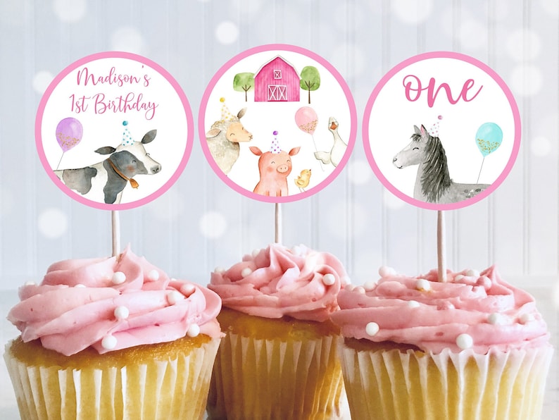 K&ouml;nnte beinhalten: Drei runde Cupcake-Topper in Rosa und Wei&szlig; mit Illustrationen von Bauernhoftieren. Die Topper zeigen eine Kuh, ein Schwein, ein K&uuml;ken, eine Gans, ein Pferd und einen Stall. Der Text auf den Toppern lautet "Madison's 1st Birthday" und "one".