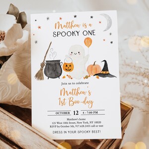 K&ouml;nnte beinhalten: Eine wei&szlig;e Einladungskarte mit orangefarbenen und schwarzen Aquarell-Illustrationen eines Geistes, eines Kessels, eines K&uuml;rbisses und eines Hexenhutes. Der Text auf der Karte lautet "Matthew is a SPOOKY ONE" und "Join us to celebrate Matthew's 1st Boo-day".