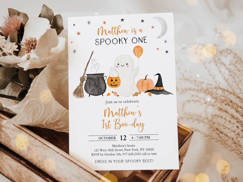 K&ouml;nnte beinhalten: Eine wei&szlig;e Einladungskarte mit orangefarbenen und schwarzen Aquarell-Illustrationen eines Geistes, eines Kessels, eines K&uuml;rbisses und eines Hexenhutes. Der Text auf der Karte lautet "Matthew is a SPOOKY ONE" und "Join us to celebrate Matthew's 1st Boo-day".