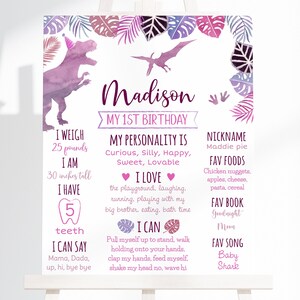 May include: A pink and purple dinosaur-themed first birthday sign with the name Madison. The sign includes details about the child's weight, height, favorite foods, and other milestones.