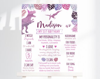 May include: A pink and purple dinosaur-themed first birthday sign with the name Madison. The sign includes details about the child's weight, height, favorite foods, and other milestones.
