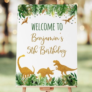 May include: Welcome to Benjamin's 5th Birthday sign with a green and gold dinosaur theme. The sign features a gold dinosaur silhouette with green foliage and gold confetti.