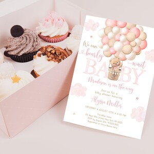May include: A pink and gold baby shower invitation with a teddy bear in a hot air balloon made of balloons. The text reads "We can bearly wait BABY Madison is on the way".