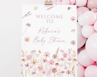 May include: A white sign on an easel with the text "WELCOME TO Rebecca's Baby Shower" in a soft pink script. The sign is decorated with watercolor flowers in shades of pink, peach, and lavender. Pink balloons are in the background.