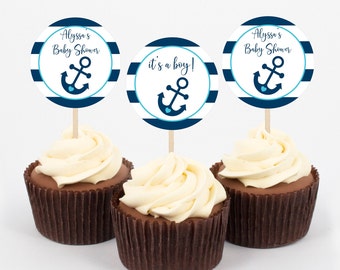 Puede incluir: Tres cupcakes con adornos de cupcakes con temática de ancla a rayas azules y blancas. Los adornos dicen "Alyssa's Baby Shower", "it's a boy!" y "Alyssa's Baby Shower".